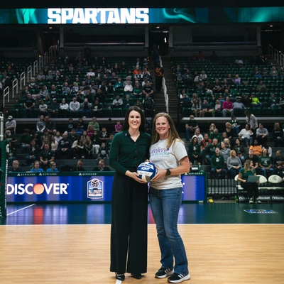 Coach Kelsay and Danielle Fenton hold a volleyball together on the Breslin Center court.