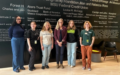 Laura Lee McIntyre and three students in front of the donor wall at the MSU Broad Art Museum