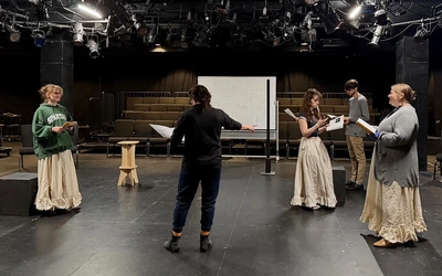 Four members of the cast and a director rehearse together on stage.