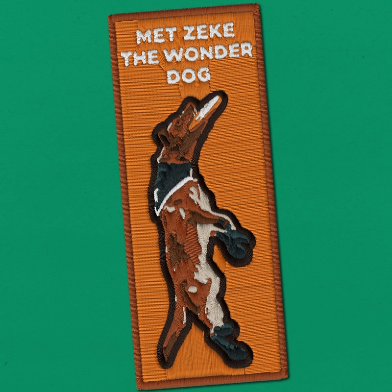 Embroidered orange patch reading "Met Zeke the Wonder Dog" with a tan and white dog catching a frisbee with a green background.