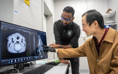 Chunqi Qian points to a medical scan on a computer monitor while reviewing the image with a colleague in a radiology lab.