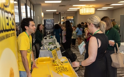 Student entrepreneur at a yellow Nanners booth speaking with attendees.