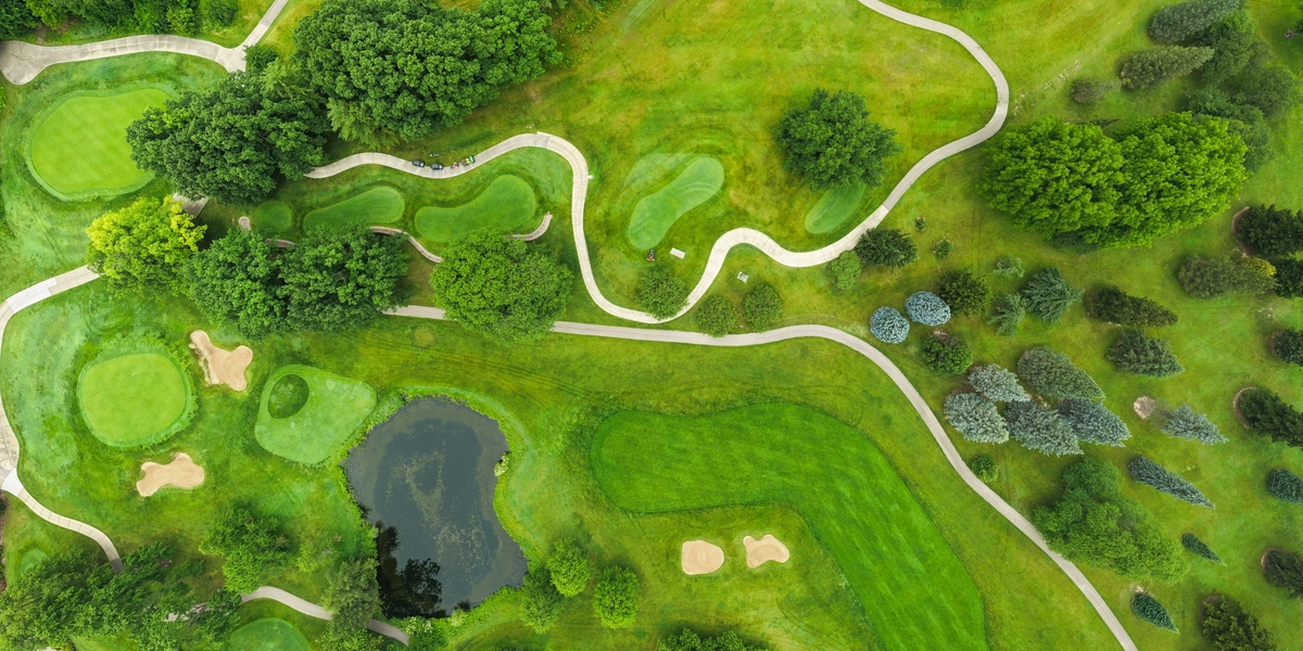 Aerial view of Forest Akers West Golf course, with sand traps, a pond, tress and perfectly mowed grasses of fairways, roughs and greens