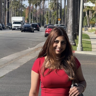 Portrait of a woman with long hair in a red top. The background is a sunny boulevard lined with palm trees.