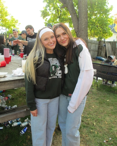 Torey Auzins, right, and her friend Jordyn stand with their arms around each other and smile at an outdoor MSU football tailgate.