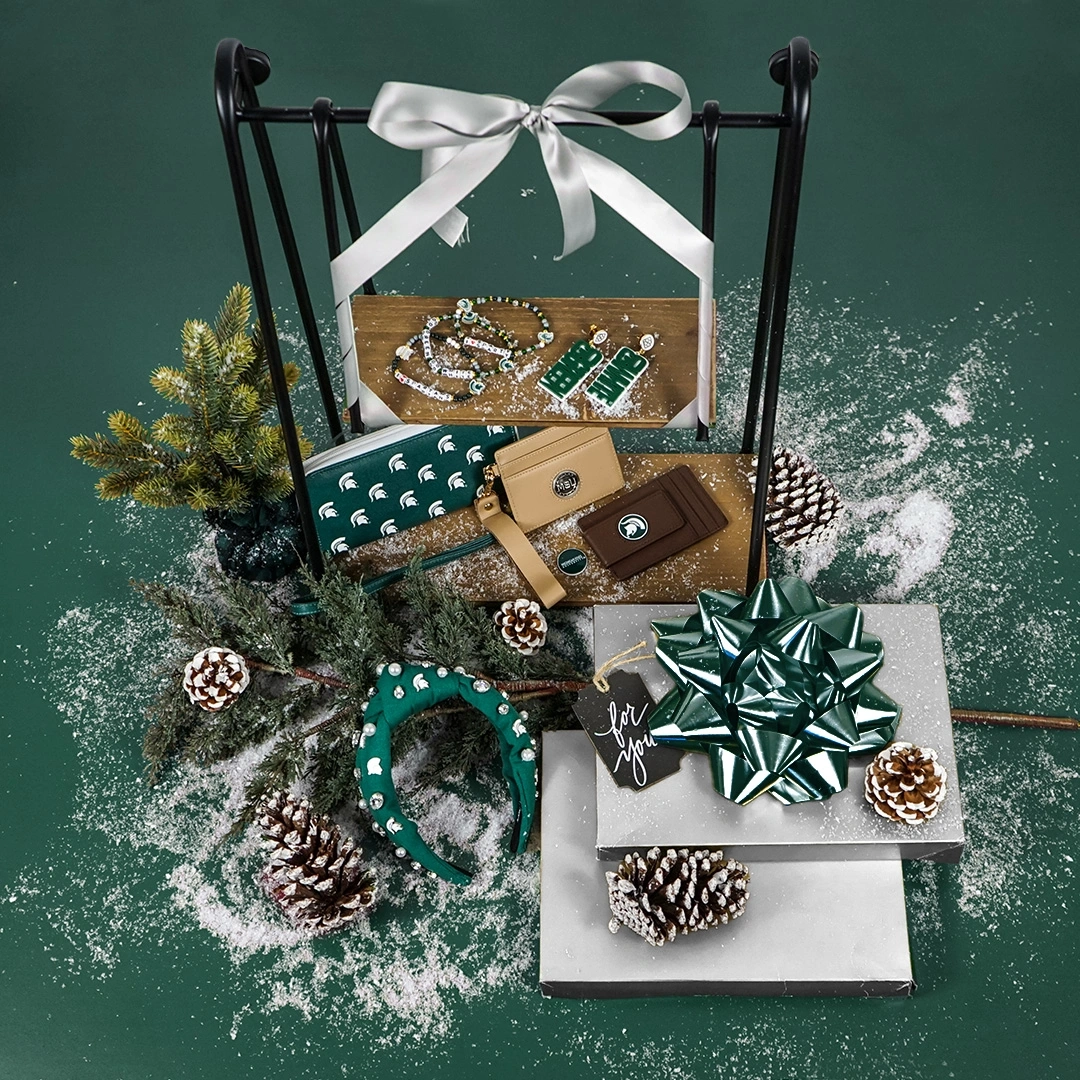 MSU-themed jewelry and accessories arranged with pinecones and faux snow.