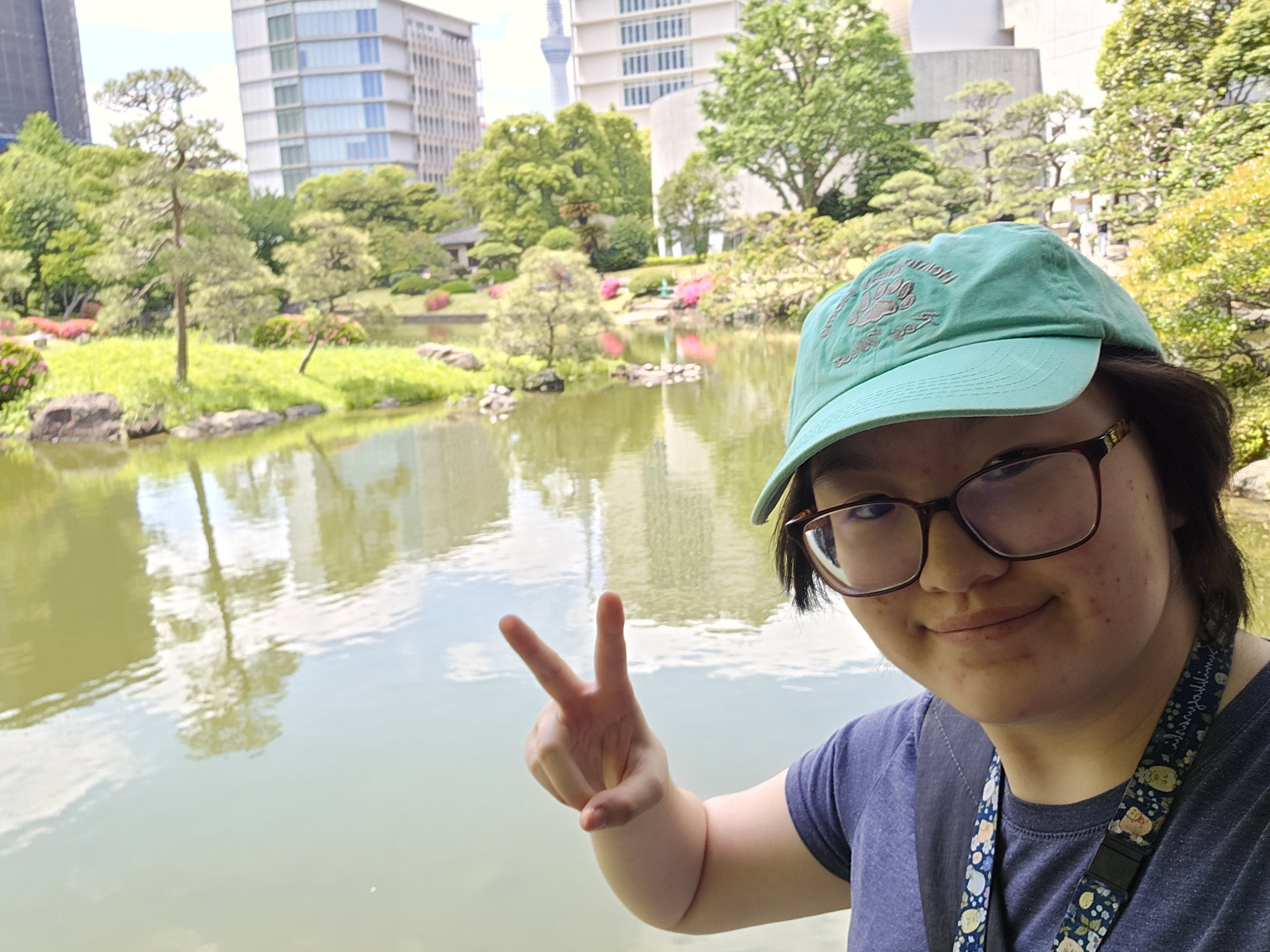 A woman makes a hand gesture in a selfie in front of a pond garden