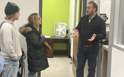 A woman and young man listen to a man talk. The man talking is gesturing with his hands.