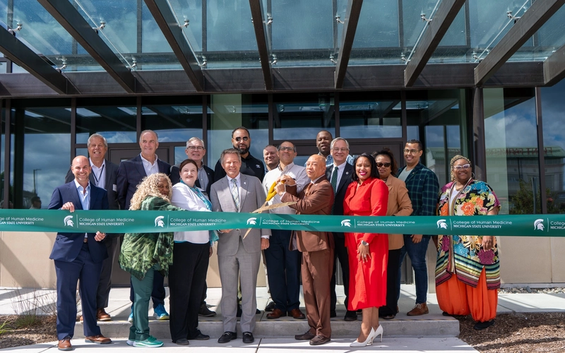 A group pose for a photo for a ribbon cutting in front of the MSU College of Human Medicine Charles Stewart Mott Department of Public Health.