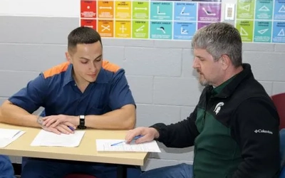 Kirk Astle sitting with a student, pointing at a piece of paper as the student looks at it.