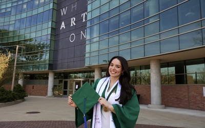 Graduate in green and white stands outside of the Wharton Center