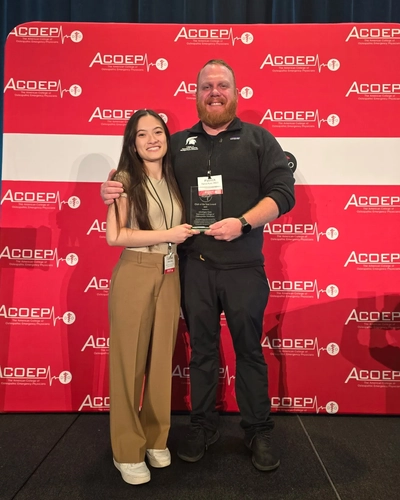 Two people pose with an award in front of event background.