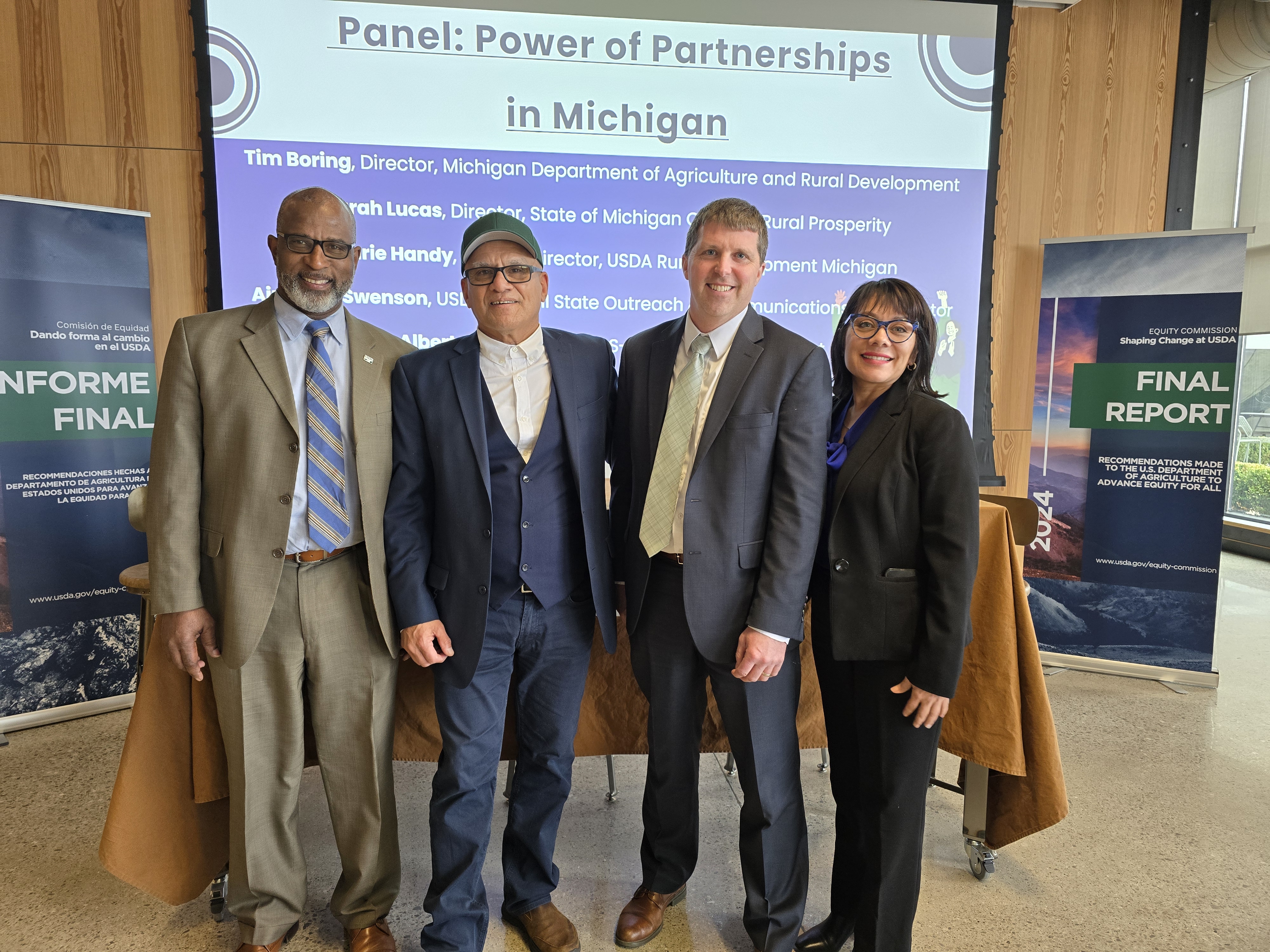 A group of men stand in front of a projection screen "Power of Partnerships in Michigan"
