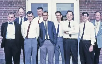 A group of men pose for photo in front of brick building.