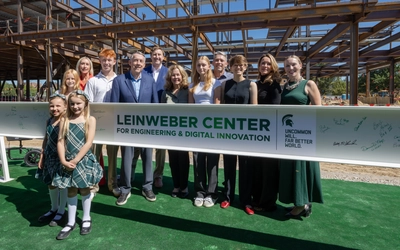 Group of people standing by a construction beam with signatures visible on the beam.