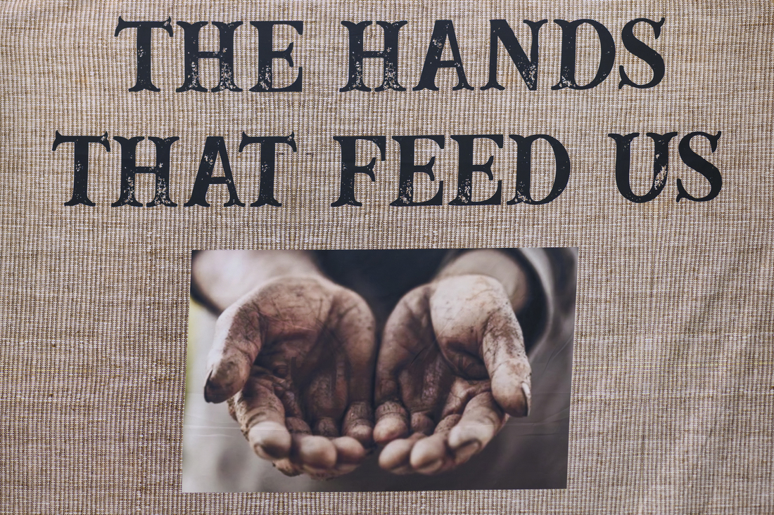 A photo backdrop with a picture of soiled hands outstretched with palms facing up and the words the hands that feed us