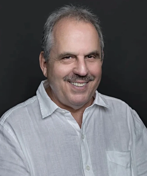 Bill Mechanic, MSU alumnus and film producer, smiling in a studio portrait against a dark background.