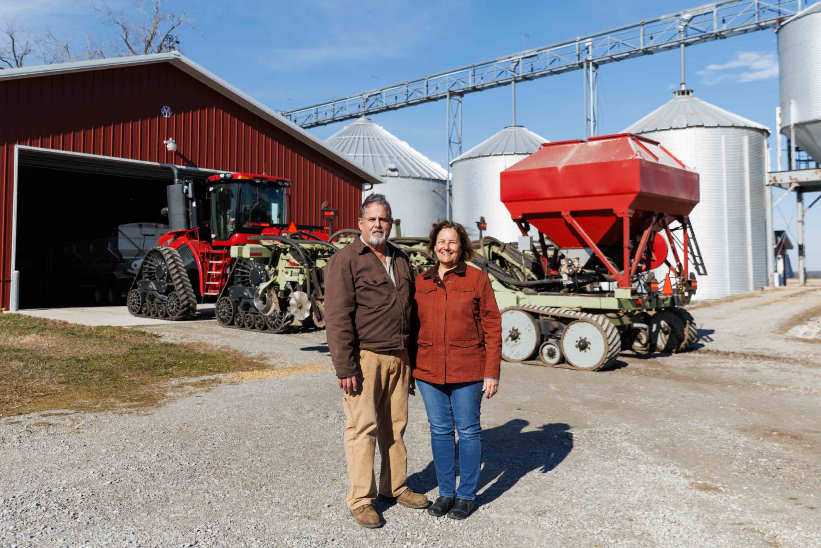 Jim and Laurie Isley, dedicated stewards of Sunrise Farms in Palmyra, Michigan, standing proudly in front of their farm's equipment and infrastructure, showcasing the real-world application of sustainable agricultural practices.