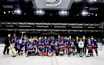 Group of hockey players and coaches pose for a photo on ice.