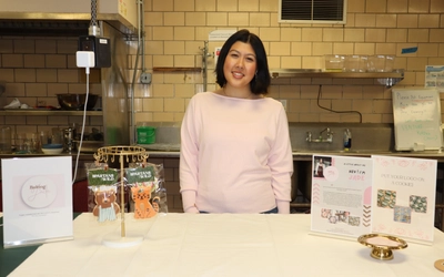 MSU senior Jade McLellan stands behind a display for her business, Baking By Jade, featuring decorated Spartan-themed cookies and promotional materials.