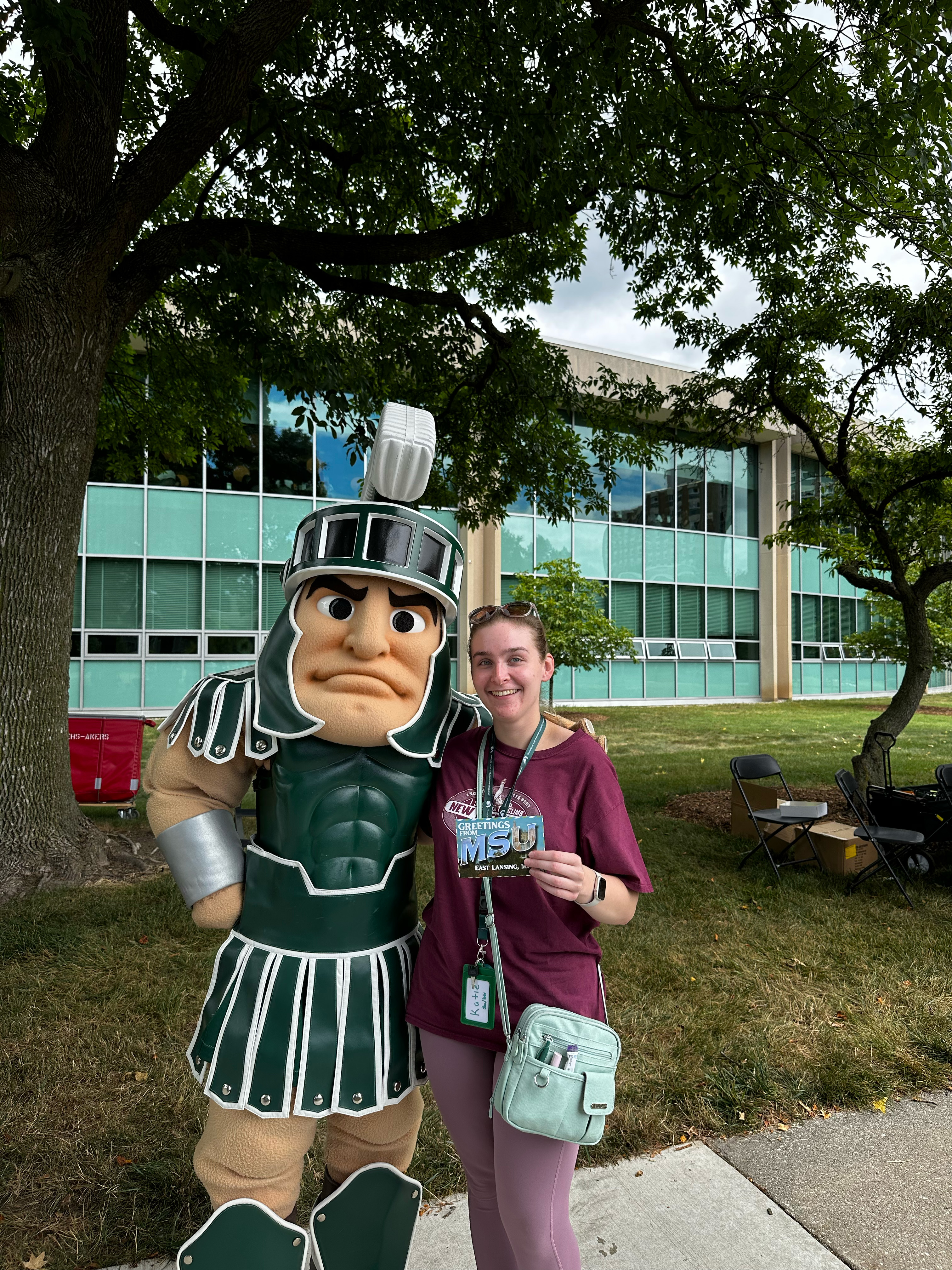 Sparty poses with a student holding an MSU postcard on campus