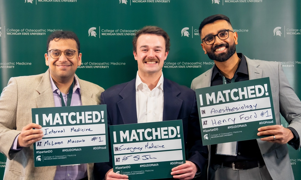 Three male medical students smiling and holding residency match signs in front of an MSU backdrop.