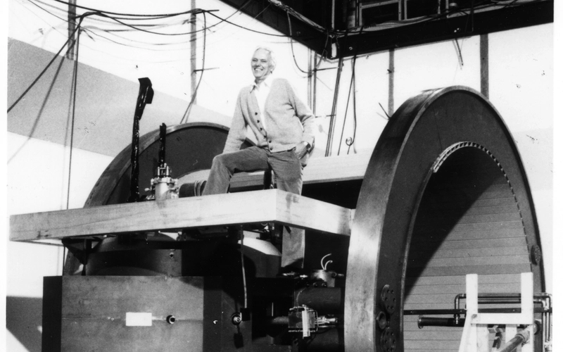 Researcher Henry Blosser and on top of the medical cyclotron posing for a photo in October 1991