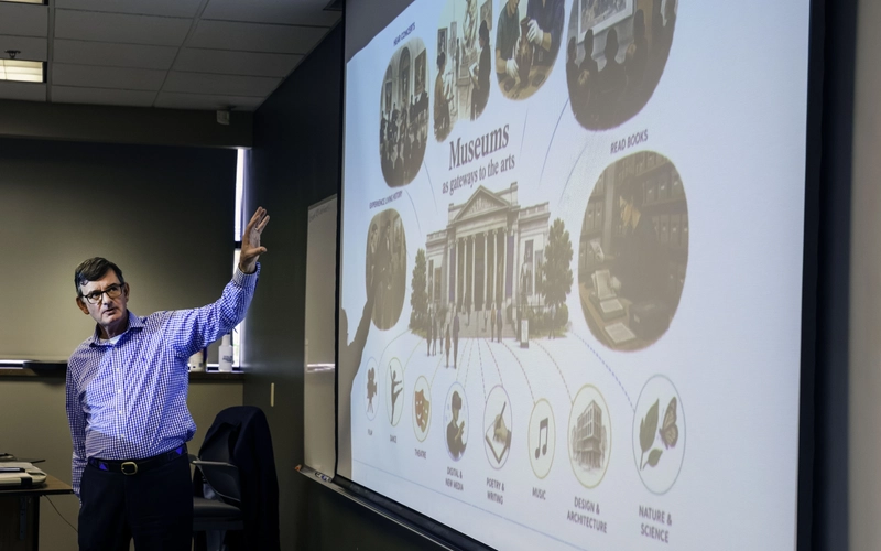 Presenter points to projected image on large white screen titled "Museums as gateways to the arts" with various images.
