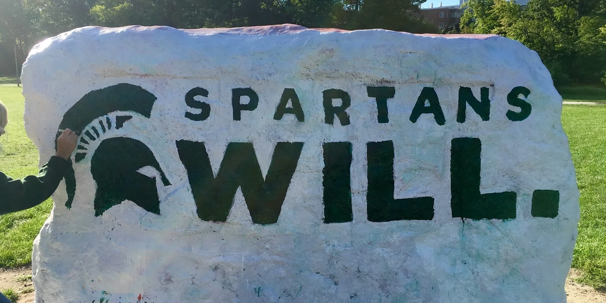 MSU Rock painted in green and white with Spartan helmet and slogan Spartans Will.