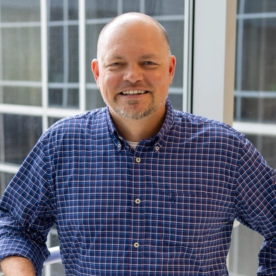 Man wearing a blue and white checkered shirt standing in front of a window