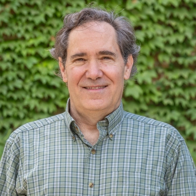 Man in a green plaid collard shirt standing in front of a wall of green vines.
