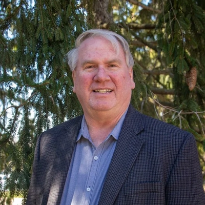 Timothy Grotjohn standing in front of a tree wearing a navy checkered jacket and blue oxford shirt.