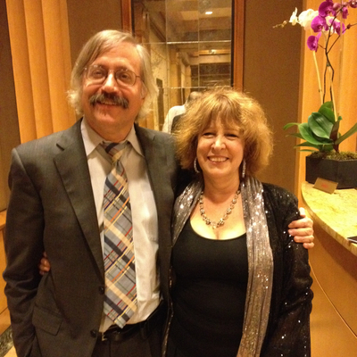 Randy Cowen (left) and his wife Phyllis Green (right) are smiling standing side-by-side with their arms wrapped around each other's shoulders.