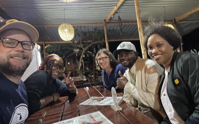 Five participants in the Michigan State University Professional Fellows Program smile while seated around a wooden table at an open-air restaurant during the fellowship exchange.