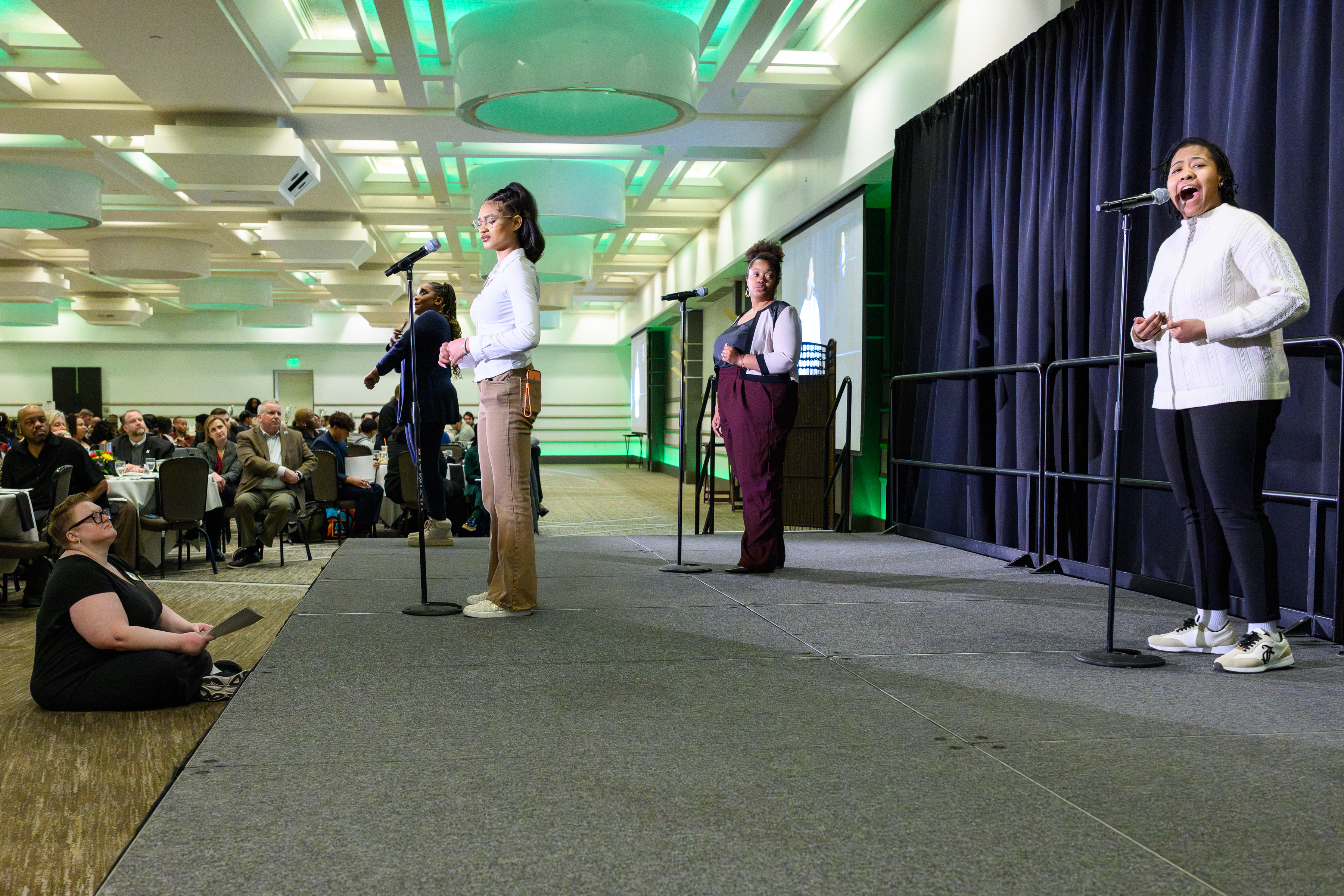 Three students perform on stage in a large banquet room