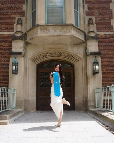 Anastassiya Kan standing in front of Mason Hall at MSU's campus holding graduation regalia.