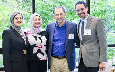 Mohammad Khalil, far right, and three other people smile for a group photo in front of large windows overlooking leafy trees.