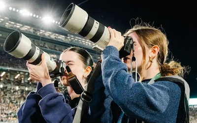 Brianna and Alexis Schmidt side-by-side, looking into their camera lenses at Spartan Stadium.