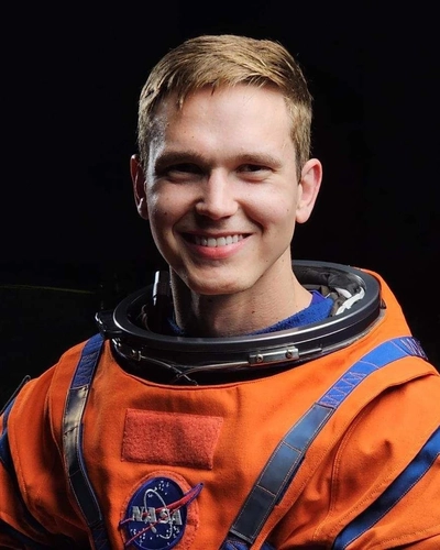 Portrait of NASA engineer Nicholas Houghton in an orange NASA space suit.