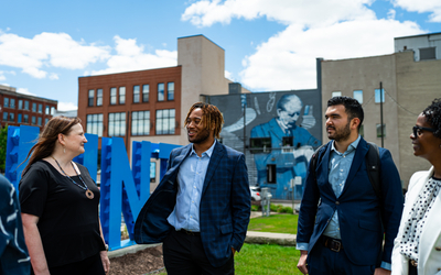 Jennifer Johnson and members of the Flint community speak with one another in front of a FLINT sign and a mural