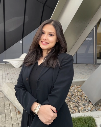 Smiling person poses in a black suit in front of a steel building