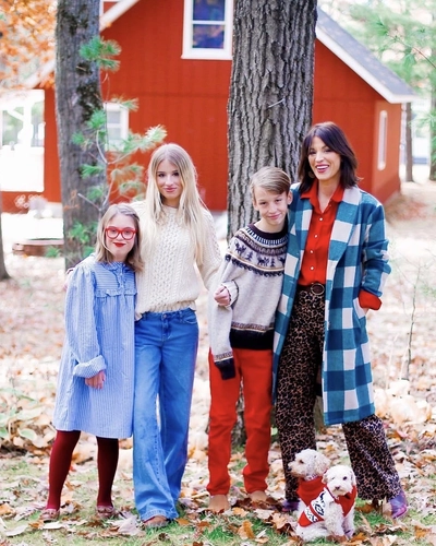 A family of four (mom and three children) poses on a fall day in front of a red barn