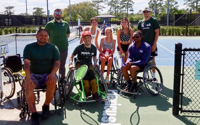 Group poses at tennis courts. Some of the tennis players are in wheelchairs