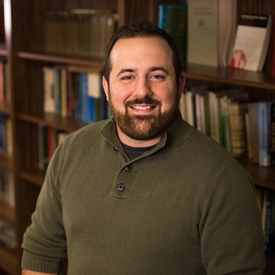 Dustin Carnahan poses in front of a bookshelf