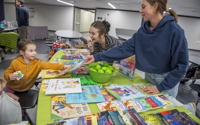 Two women pass out books ans stickers to a small child.