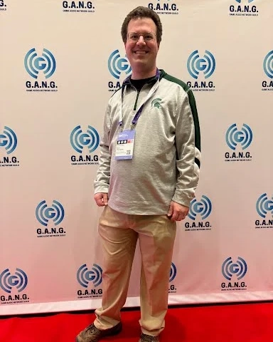 Ryan Thompson poses on the red carpet for the Games Developers Conference with a screen with logos for G.A.N.G.