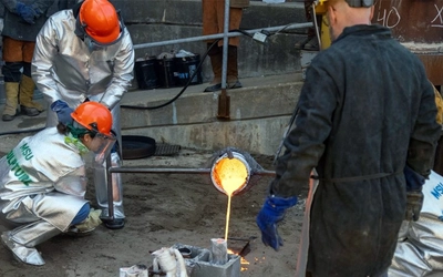 MSU Ceramics Instructor Mackenzie Sheehan-D’Arrigo helps pour molten iron into molds while students observe.