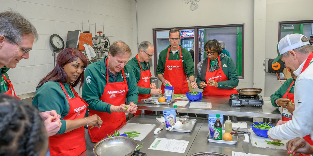 People in red aprons in a kitchen peeling fruits and vegetables