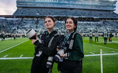 Brianna and Alexis Schmidt holding their equipment and posing together on the field at Spartan Stadium.