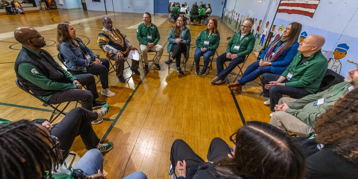 A group of people sit in a circle in a gymnasium